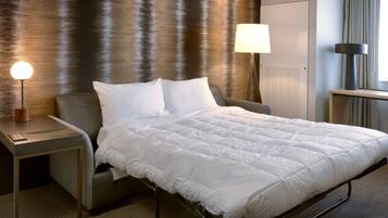 A neatly made bed with white bedding, a bedside table with a lamp, and a wall with a textured pattern.