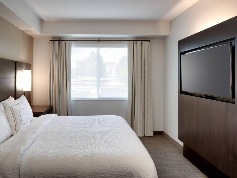 Habitación de hotel con una cama grande, televisión de pantalla plana, mesita de noche y ventana con cortinas.