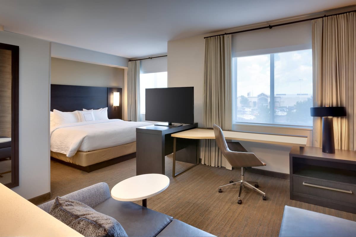 Ein modernes Hotelzimmer mit Bett, Schreibtisch, Stuhl und einem großen Fenster mit Blick auf die Stadt.