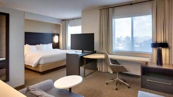 A modern hotel room with a bed, desk, chair, and a large window offering a city view.