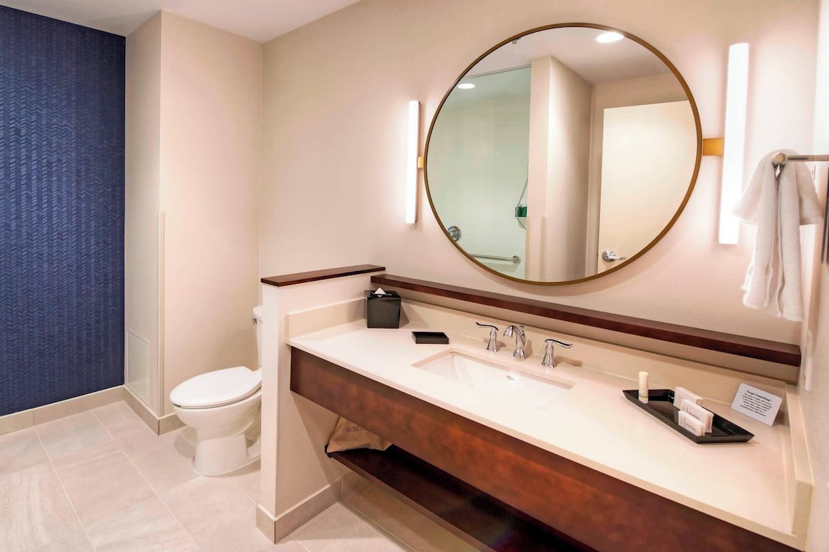 Een moderne badkamer met een wit wastafelmeubel, een ronde spiegel en een toilet.
