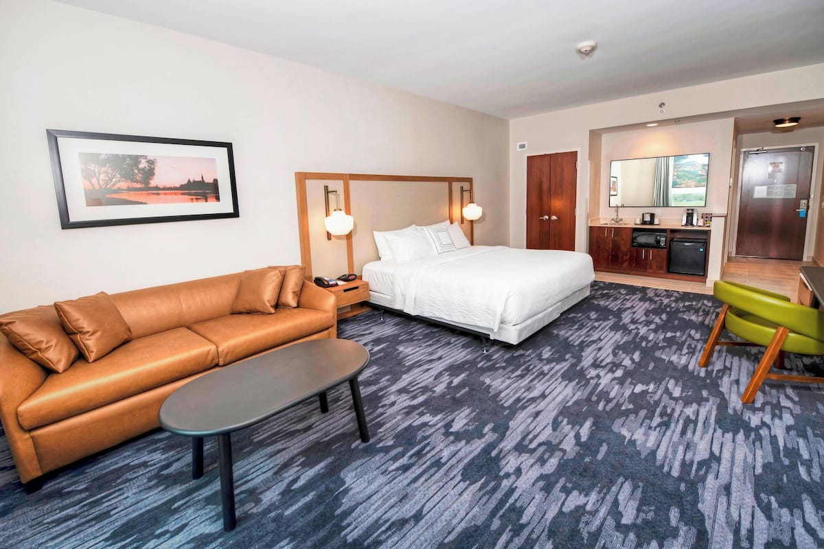 Een hotelkamer met een bed, een bank, een kleine tafel, een bureau met een magnetron en een spiegel.