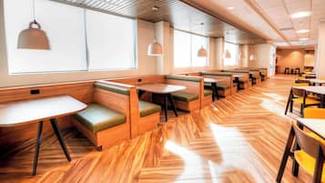 A modern restaurant with wooden flooring, green cushioned booths, and pendant lighting.