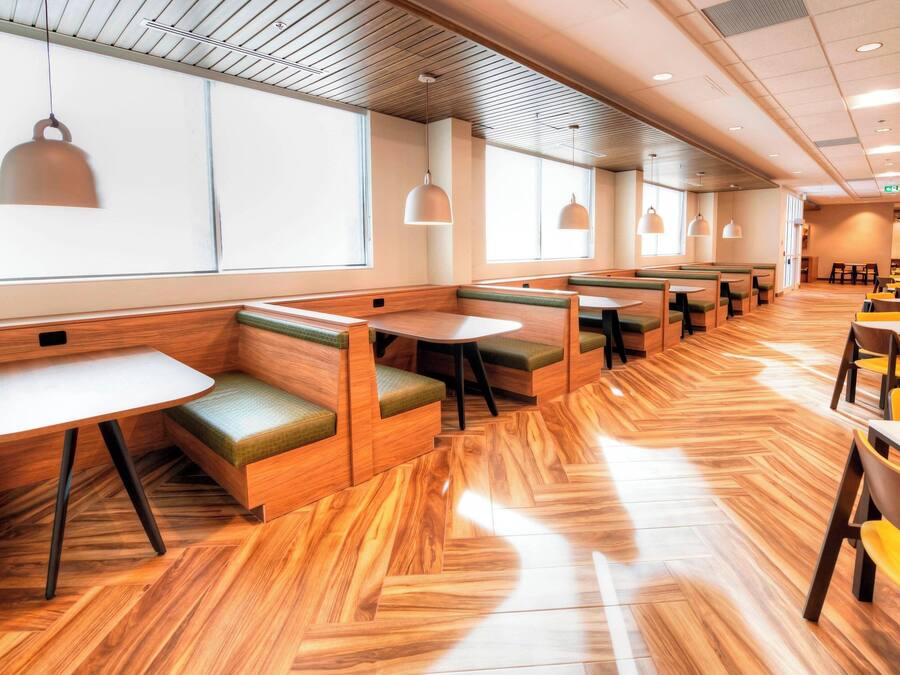 A modern restaurant with wooden flooring, green cushioned booths, and pendant lighting.