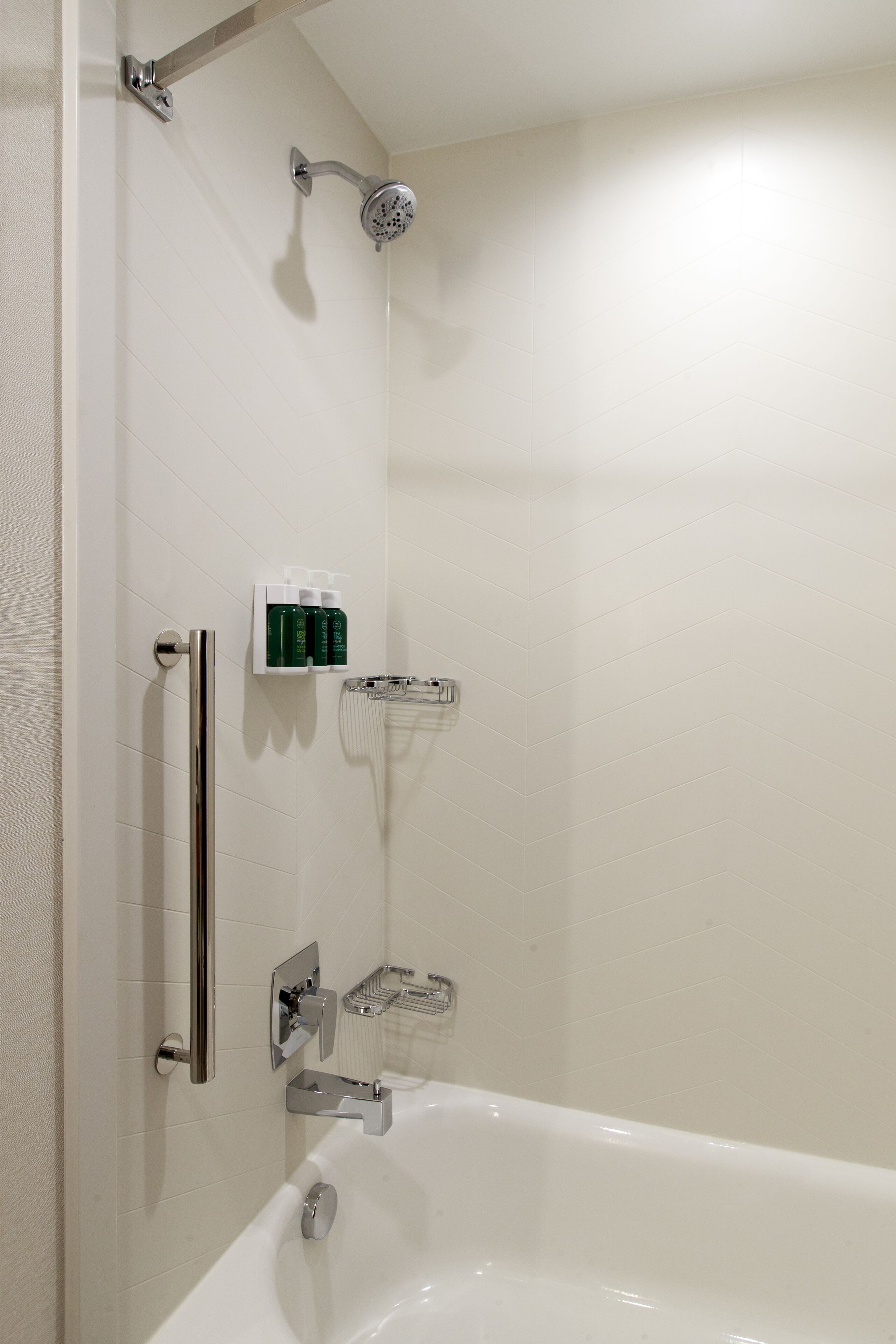 A modern bathroom with a walk-in shower, a grab bar, a handheld showerhead, and a white bathtub.
