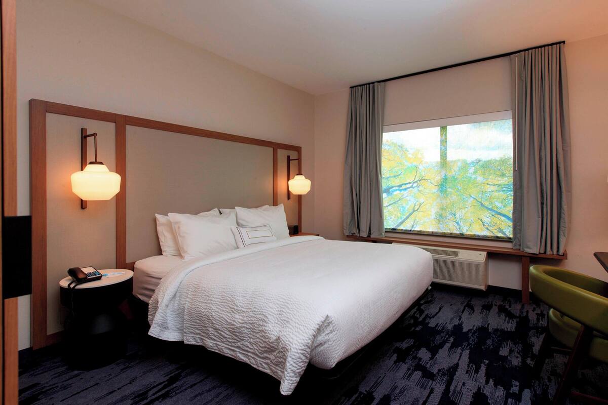 A hotel room with a large bed, two bedside lamps, a desk with a chair, and a window with curtains.