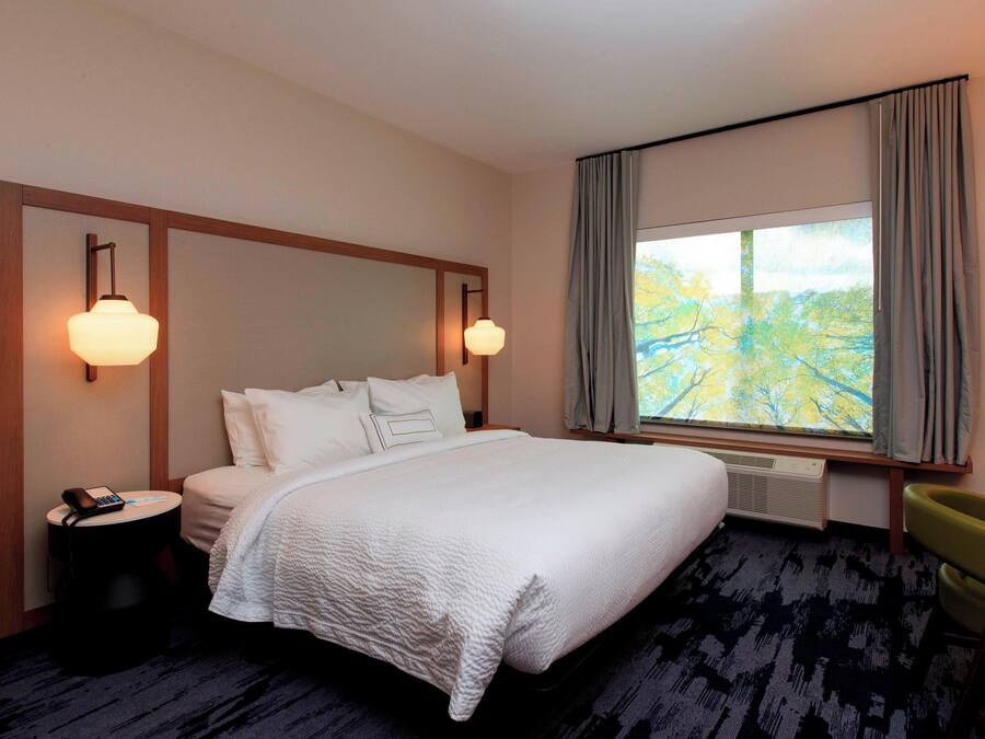 Habitación de hotel con una cama grande, dos lámparas de noche, un escritorio con una silla y una ventana con cortinas.