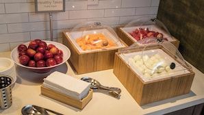 A buffet with various fruits and yogurt containers, including apples, oranges, and bananas.