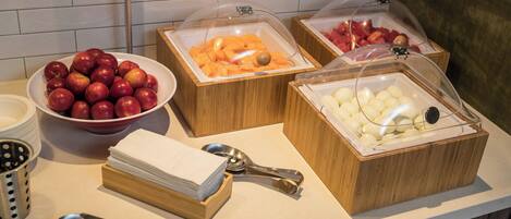 Un buffet proposant une variété de fruits et de yaourts, notamment des pommes, des oranges et des bananes.
