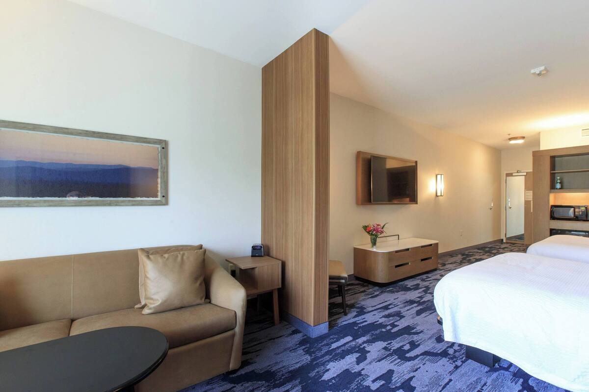 A hotel room with a bed, a sofa, a small table, a TV, and a painting on the wall.