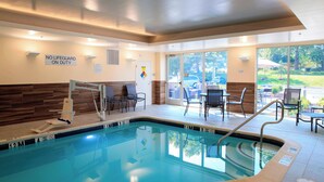 An indoor swimming pool with a lifeguard chair, chairs around the pool, and a sign stating "No Lifeguard on Duty".