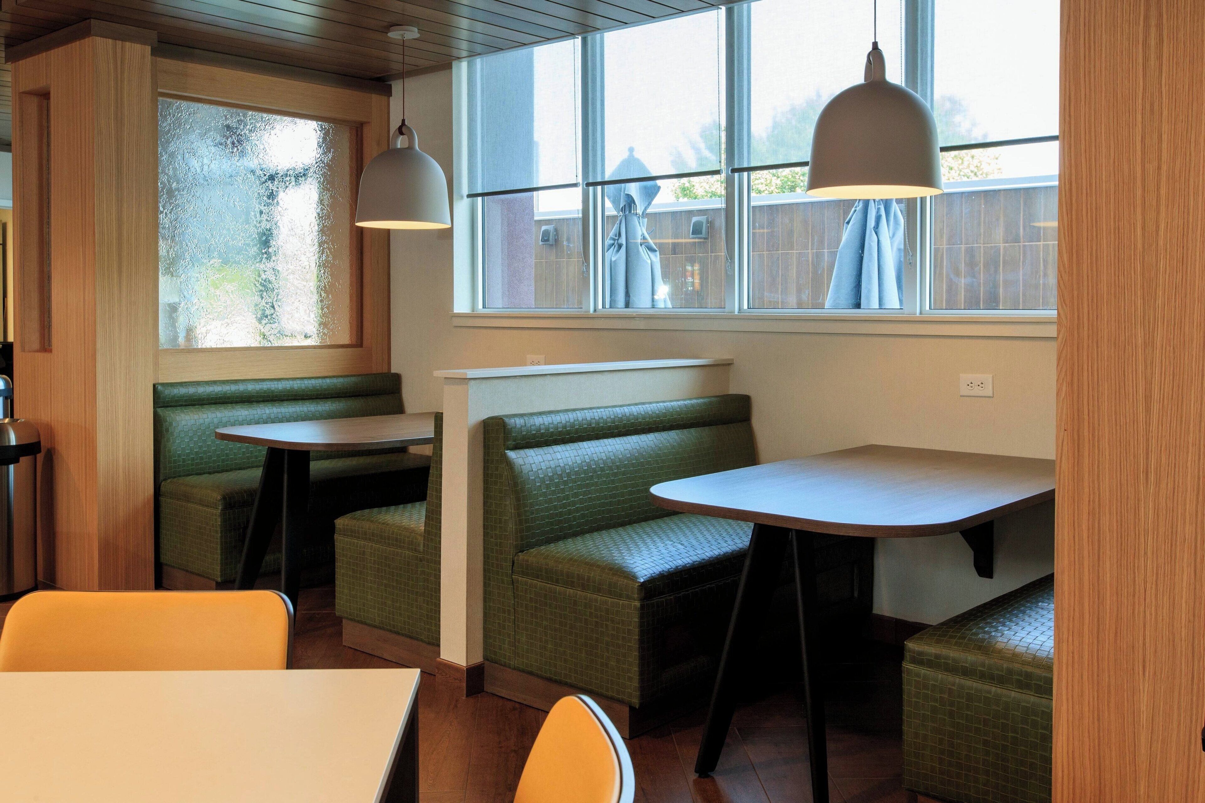 A restaurant with booth seating and tables, large windows with views, and pendant lighting.
