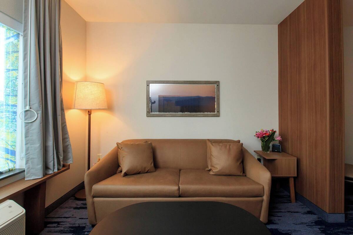 A hotel room with a sofa, a lamp, a small table with flowers, and a framed picture on the wall.