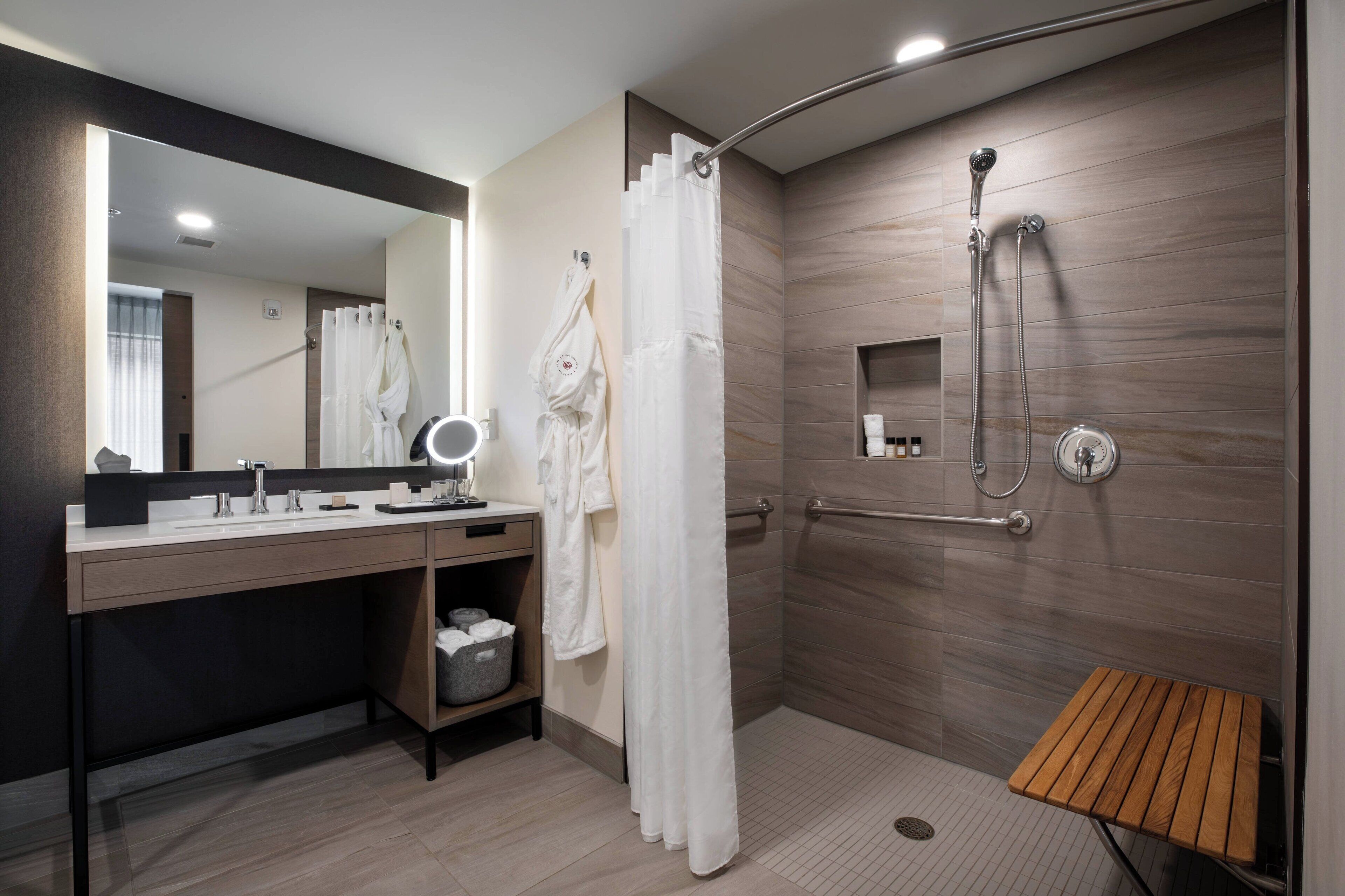 A modern bathroom with a shower, a vanity with a mirror, and a wooden bench.