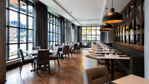 Un restaurante moderno con mesas largas, cortinas oscuras y grandes ventanales con vista a la ciudad.