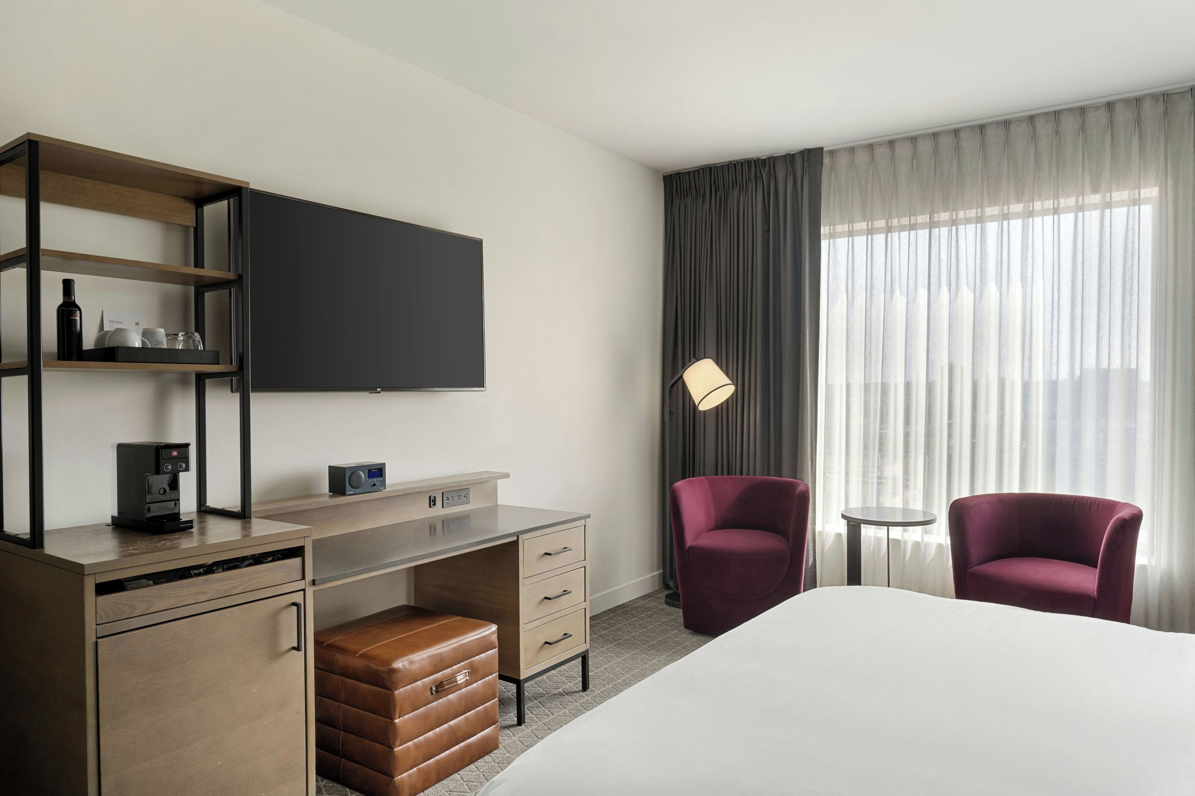Een hotelkamer met een bed, een bureau met een koffiezetapparaat, een televisie, twee stoelen en een lamp.