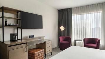 Een hotelkamer met een bed, een bureau met een koffiezetapparaat, een televisie, twee stoelen en een lamp.