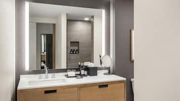 A modern bathroom with a double sink vanity, a large mirror, and a small vanity table with toiletries.