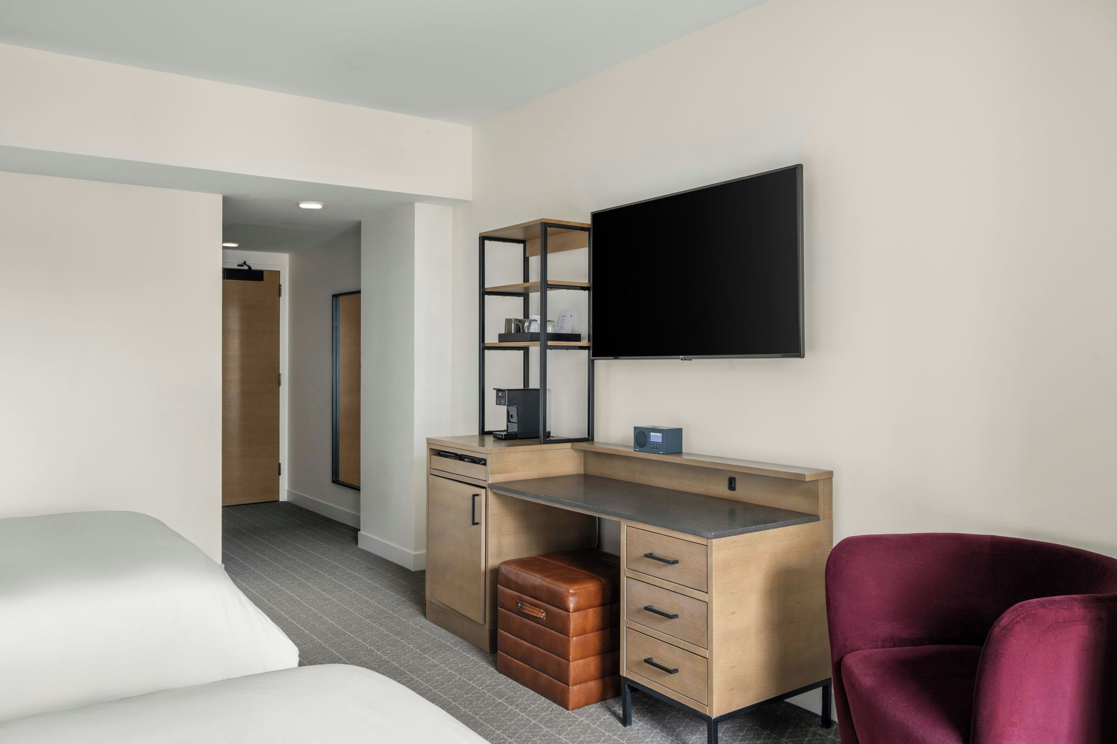 A modern hotel room with a bed, a desk with a computer, a flat-screen TV, and a red chair.
