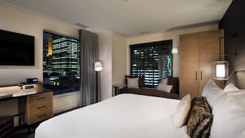 Une chambre d’hôtel avec un grand lit, un bureau, une chaise, une télévision, une fenêtre donnant sur la ville et une armoire.