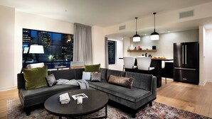 Un salón moderno con un sofá gris, una mesa de centro y vistas a la ciudad a través de amplias ventanas.