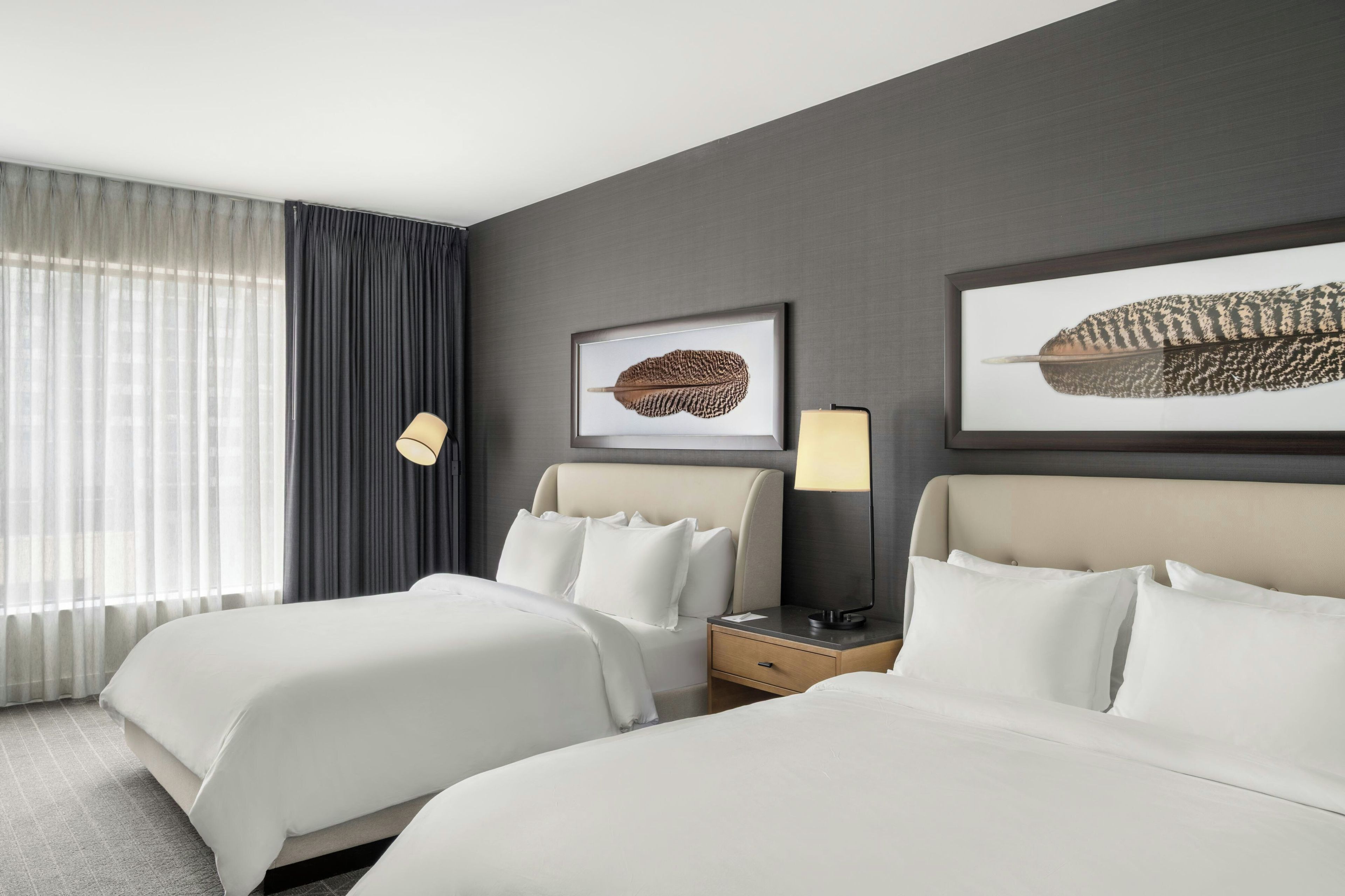 A hotel room with two beds, a nightstand, a lamp, and two framed pictures on the wall.