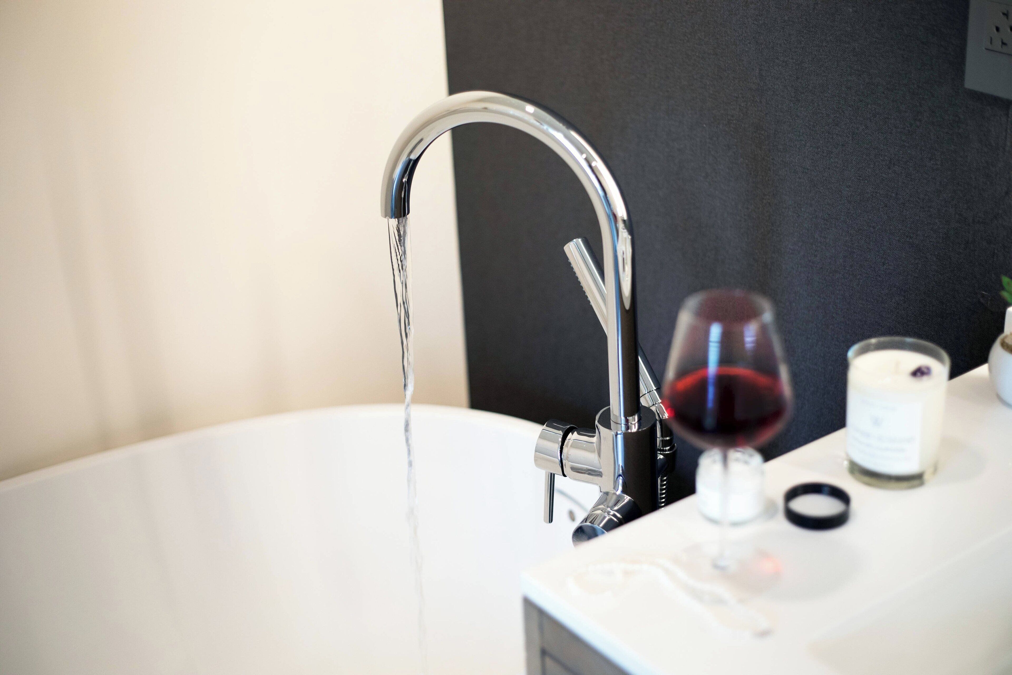 Un lavamanos de baño con grifo cromado, una copa de vino tinto y una vela sobre la encimera.