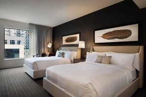 Ein Hotelzimmer mit zwei Betten, einem großen Fenster mit Vorhängen, Blick auf ein Gebäude und Kunstwerken an den Wänden.
