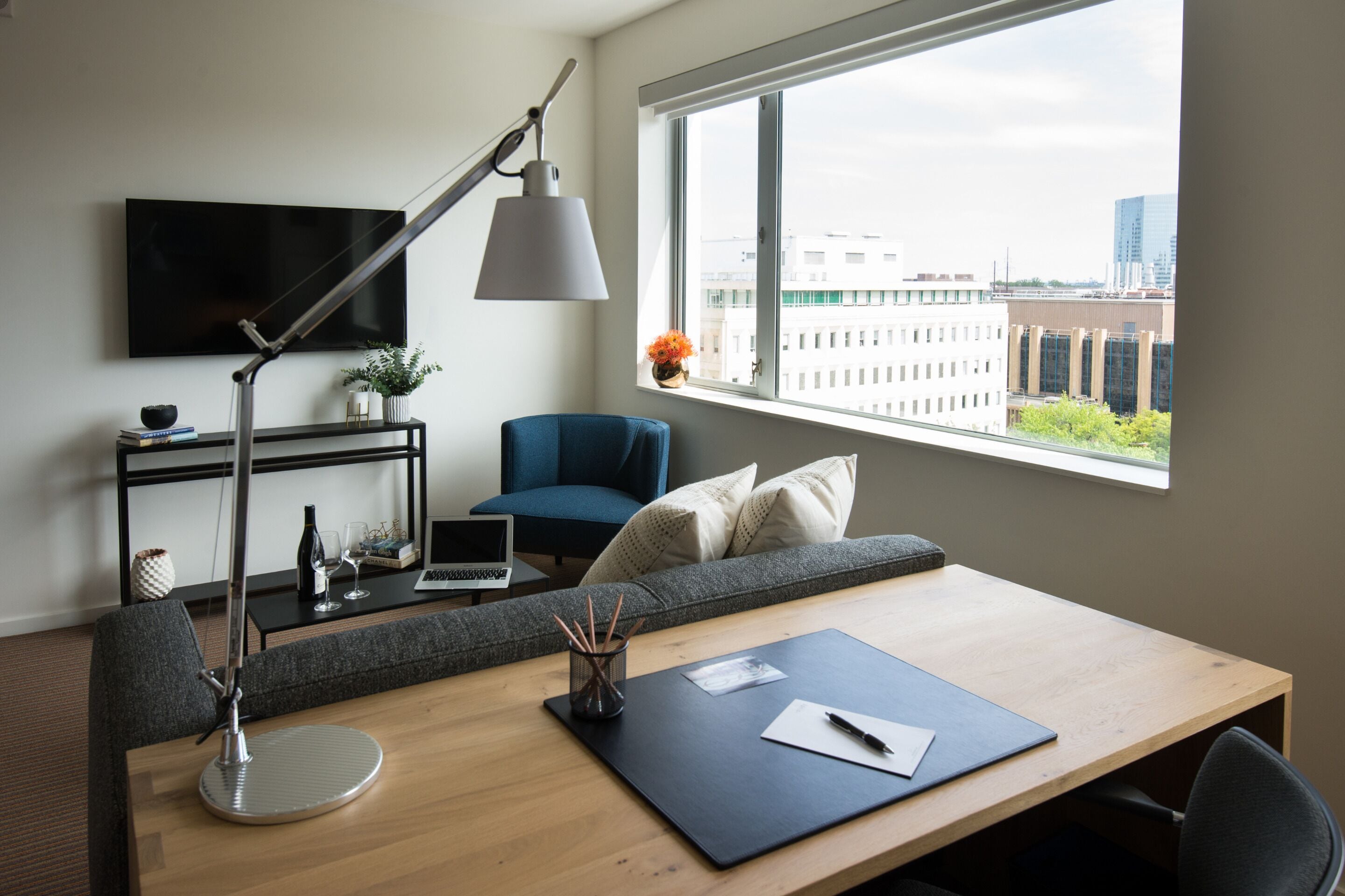 A modern room with a desk, chair, sofa, TV, and a window with a city view.
