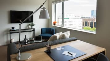 Een moderne kamer met een bureau, stoel, bank, televisie en een raam met uitzicht op de stad.