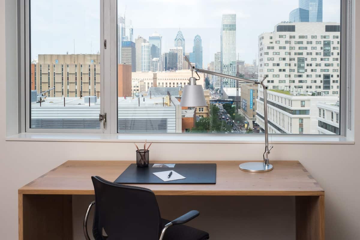 A desk with a chair and a lamp, a window with a view of a cityscape.
