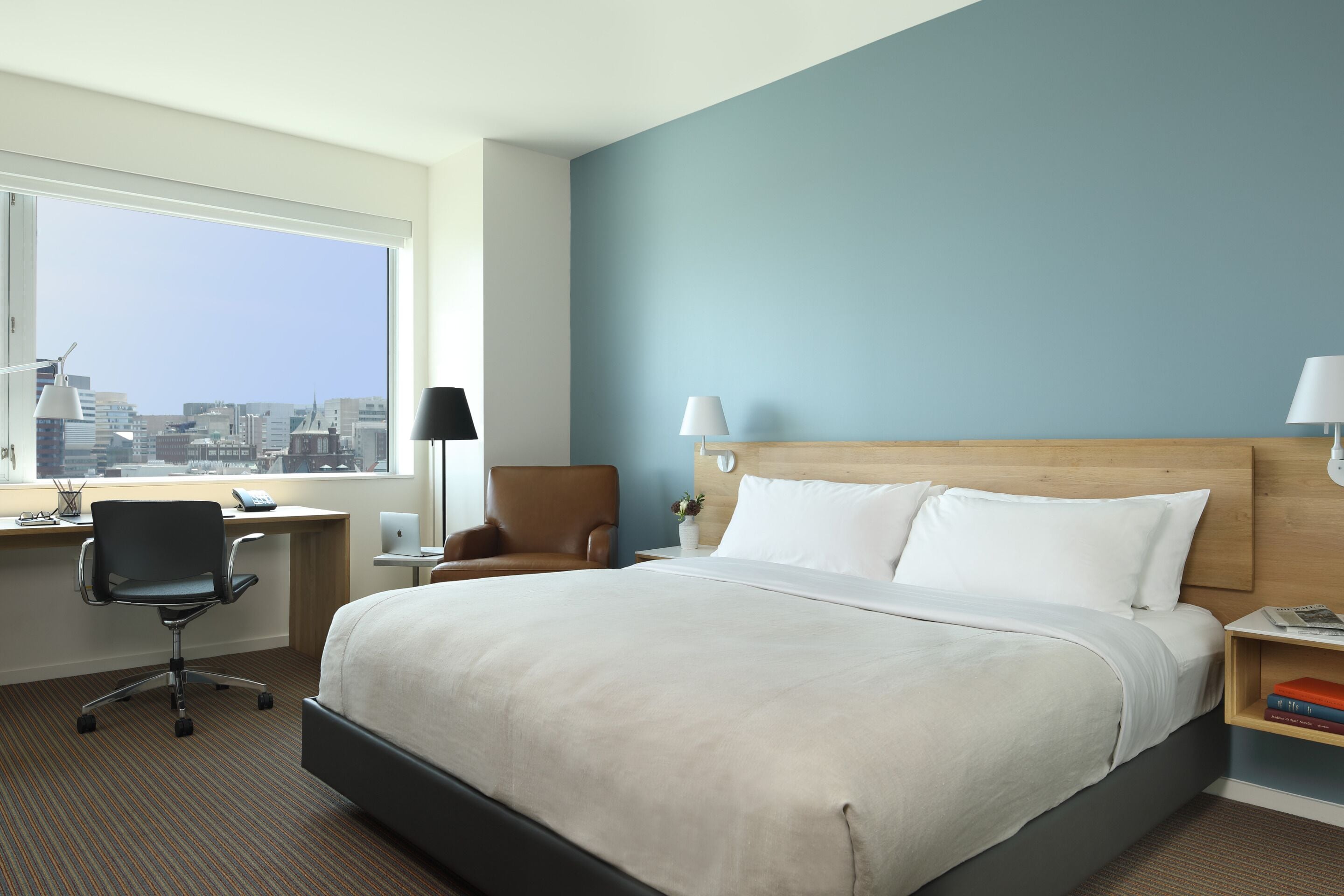 Une chambre d’hôtel avec un grand lit, un bureau avec une chaise, une lampe, une table de chevet et une vue sur la ville.