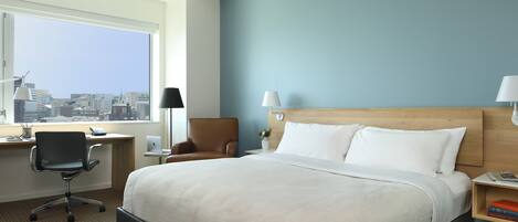 Une chambre d’hôtel avec un grand lit, un bureau avec une chaise, une lampe, une table de chevet et une vue sur la ville.