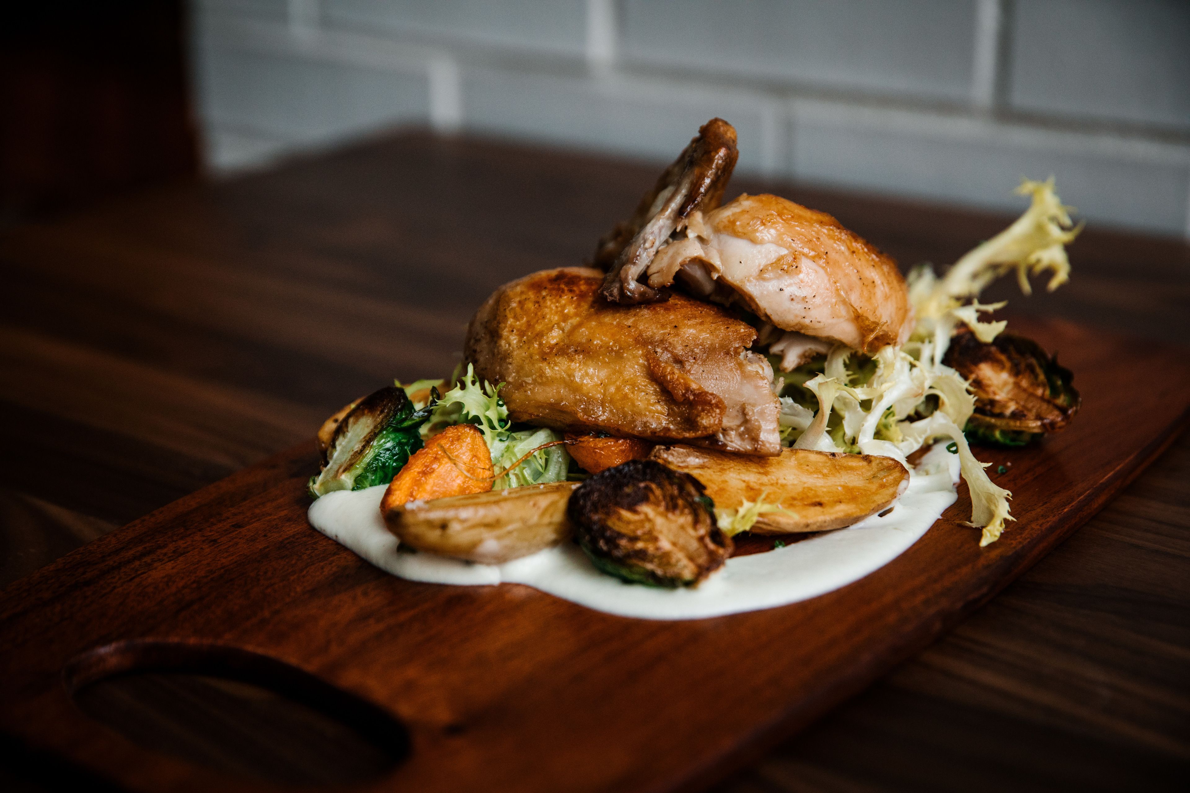 Una mesa de madera con un pollo asado, verduras y salsa cremosa.