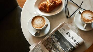 A table with a croissant, two cups of coffee, a pair of glasses, and a newspaper.