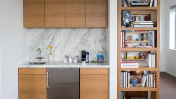 Uma cozinha moderna com armários de madeira, painel de fundo de mármore e uma estante embutida repleta de livros e objetos decorativos.