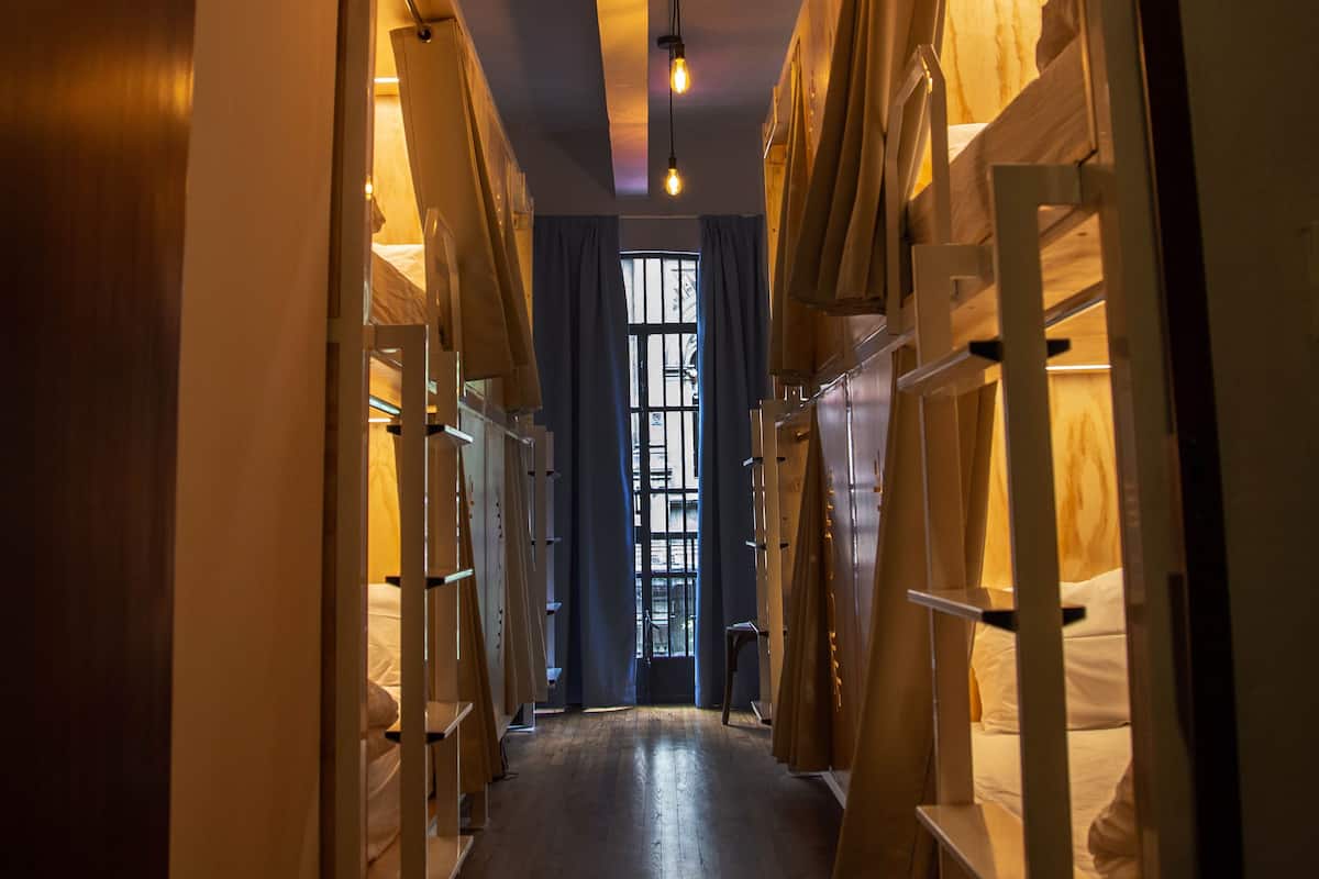 A narrow hallway with bunk beds on either side, wooden floors, and a hanging light fixture.