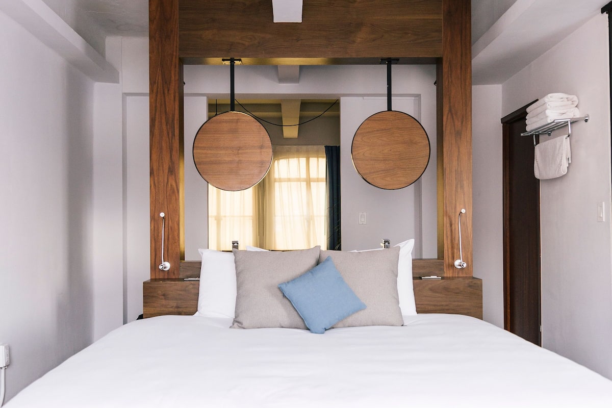 A modern bedroom with a large bed, wooden headboard, and two round wall sconces.