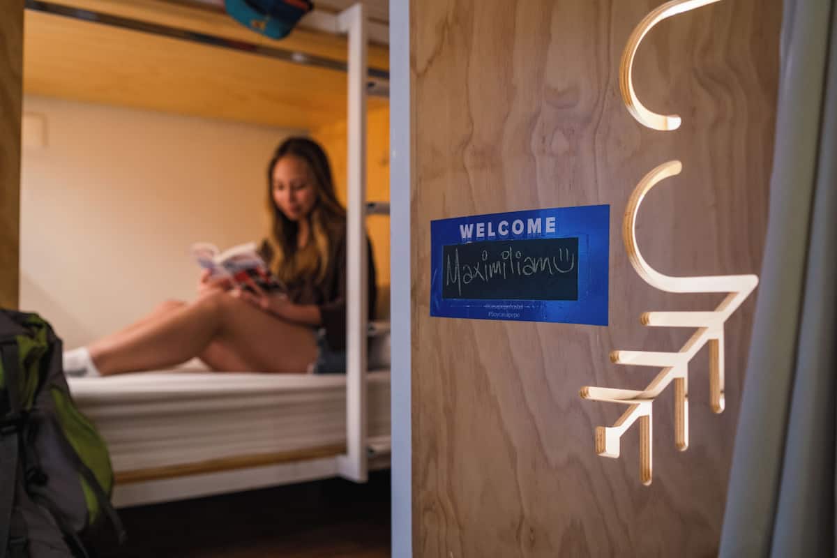A room with a bed, a person reading a book, and a welcome sign on the wall.