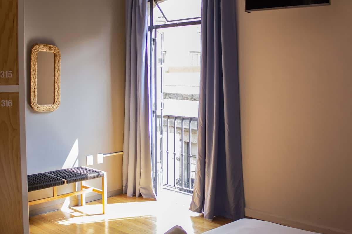 A hotel room with a bed, a chair, a TV, and a balcony with curtains.