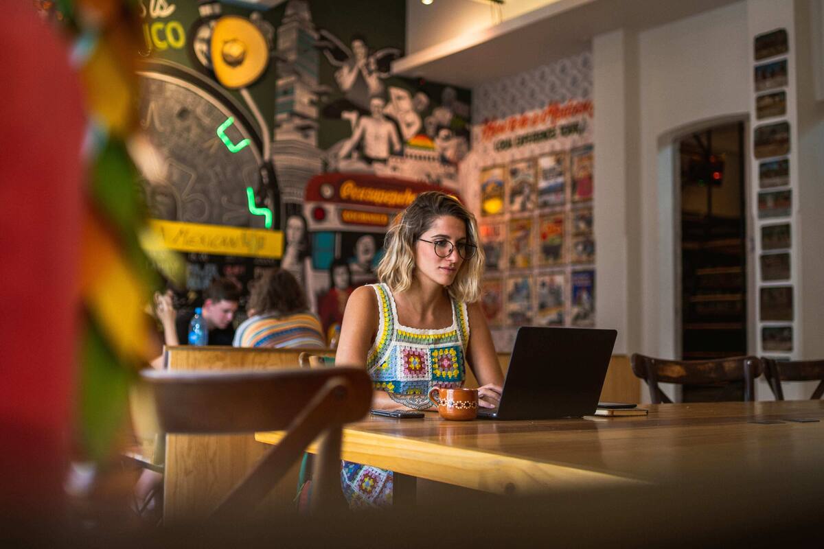A person working on a laptop at a wooden table in a cafe with a mural on the wall.