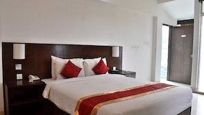 A hotel room with a large bed, two bedside tables, a nightstand, a red and gold bed runner, and a window with a view. - Inani Royal Resort (Cox's Bazar)