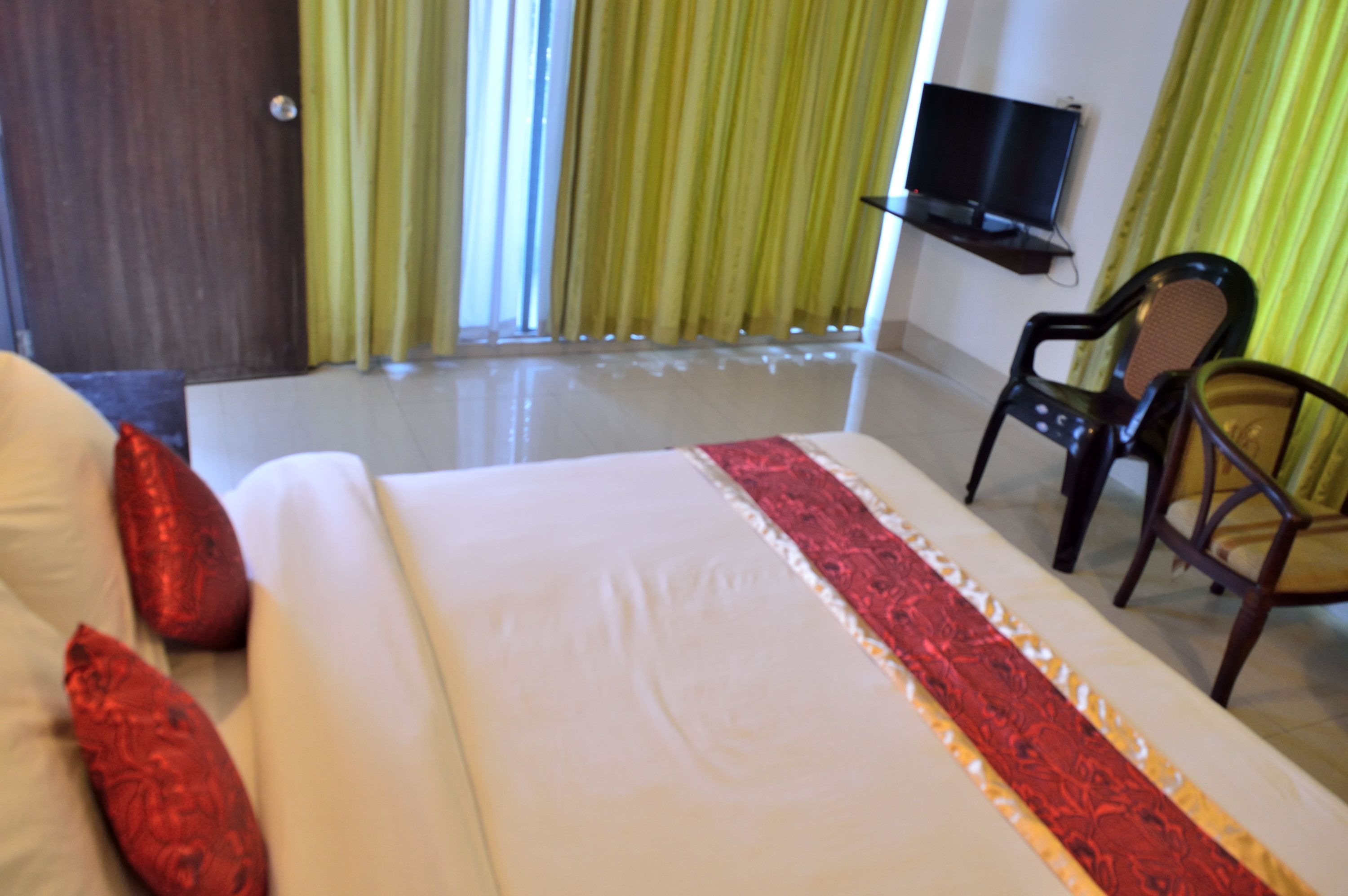 Una habitación de hotel con una cama, un televisor montado en la pared y dos sillas.