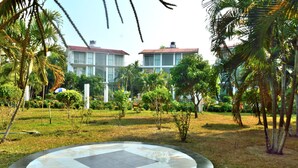A courtyard with a circular tiled area, surrounded by palm trees and greenery, leading to a building with a red roof. - Inani Royal Resort (Cox's Bazar)