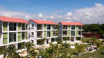 A row of white buildings with red roofs, surrounded by palm trees and a clear sky.