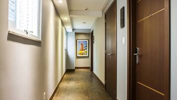 A long, narrow hallway with wooden flooring, white walls, and a large window on the left. There are doors on both sides and a framed picture on the wall.