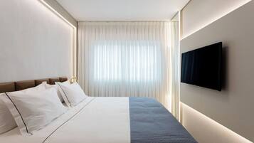Una habitació d'hotel moderna amb un llit ben fet, un televisor de pantalla plana fixat a la paret i un gran finestral amb cortines transparents.
