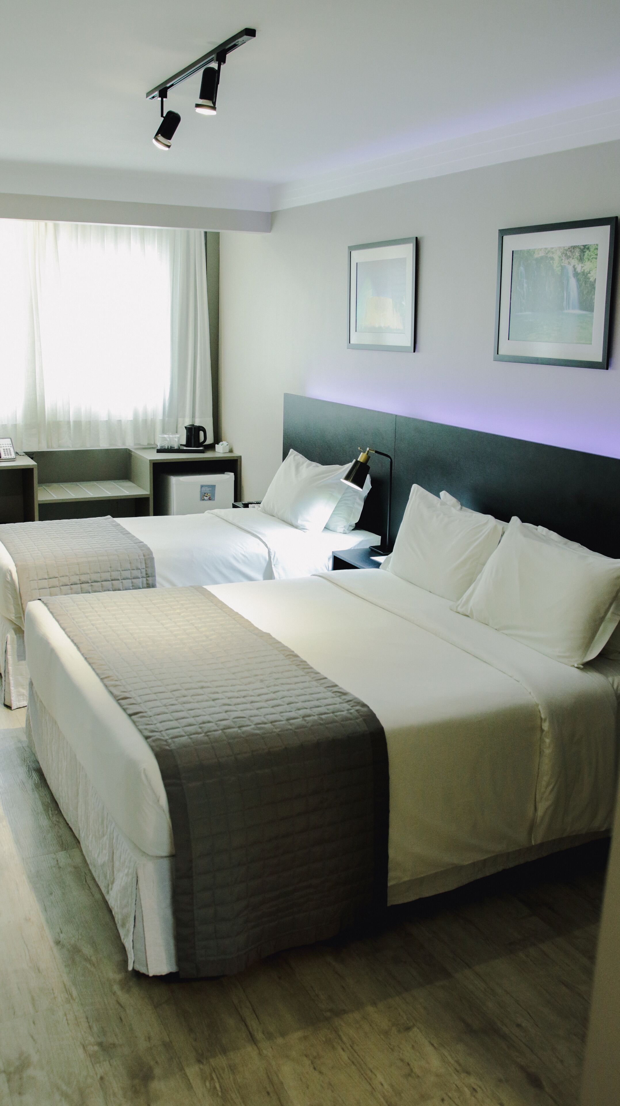 A hotel room with two beds, a nightstand, a lamp, and a framed picture on the wall.