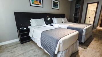 A hotel room with two beds, a nightstand, a desk, and a bookshelf.