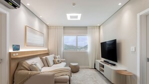 A modern living room with a sofa set, a TV, and a large window with a view of the outdoors. - Santa Inn Hotel (Balneário Camboriú)
